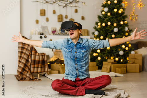 Technology, augmented reality, winter, christmas and people concept - happy young man with virtual headset or 3d glasses playing video game at home over snow