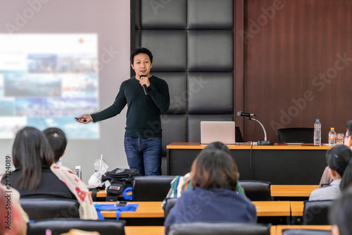 Asian Speaker or lecture with casual suit on the stage presenting via projector screen in the conference hall or seminar meeting room to Audience, business education and Seminar concept