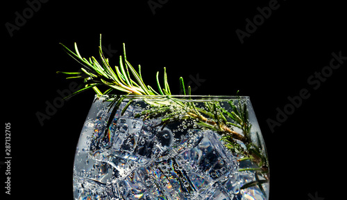 Alcoholic cocktail with ice, soda and rosemary on a black background