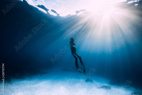 Freediver woman with fins swim underwater in sea.
