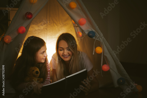 mother reading a book to her daughter indoors before going to bed