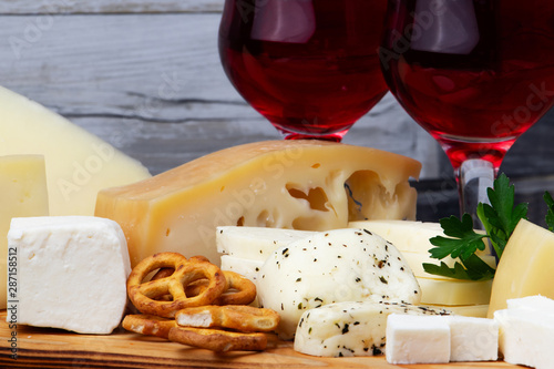 Different types of cheeses with a glass of wine on a wooden cutting board