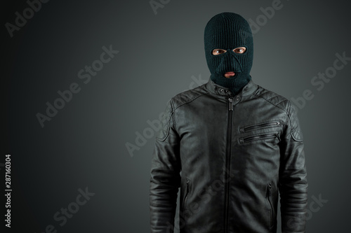 Robber, thug in a balaclava on a black background. Robbery, hacker, crime, theft. Copy space.