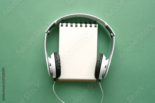 Song lyrics mockup. Music playlist. Blank page notepad and headphones on a green flat lay background.