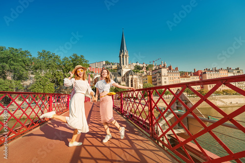 Two happy mixed race girls having fun and jumping on a bridge, while travelling in Lyon city in France
