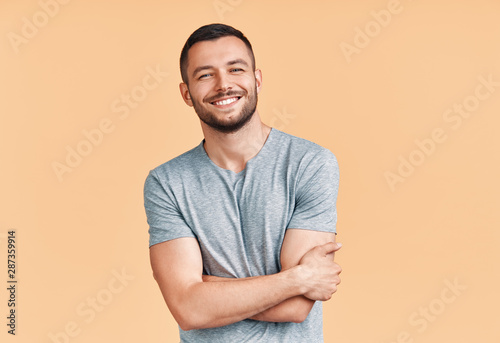 Happy smiling handsome man with crossed arms looking to camera over beige background