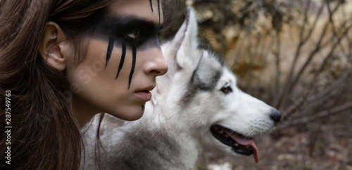Close-up portrait of a woman hunter with war paint on her cheeks against the backdrop of a wolf face