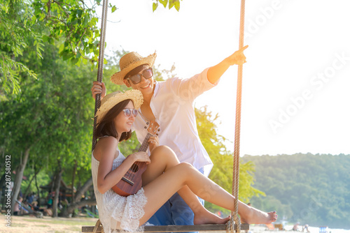 Romantic lifestyle asian couples lover playing an ukulele on the hammock. relax and honeymoon in luxury resort near the beach. Thailand. Summer,Travel, Valentine Concept.