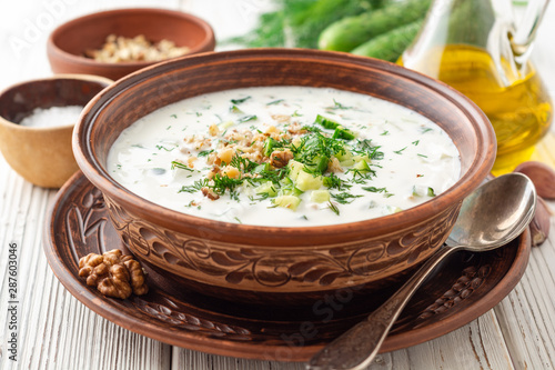 Traditional bulgarian cold summer soup tarator with yogurt, dill, cucumber and walnuts in ceramic bowl on wooden table. Selective focus.