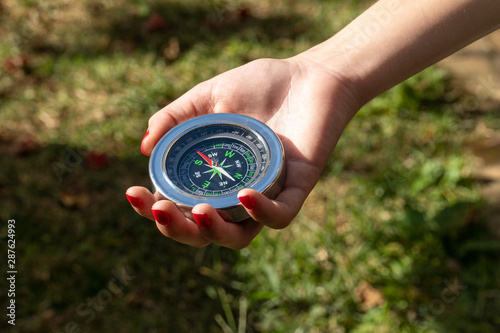 Close up of young girl hand holding a vintage chinese compass in park with grass in background on sunny summer day. Travel, adventure, freedom, technology, trekking, map and orientation concept.