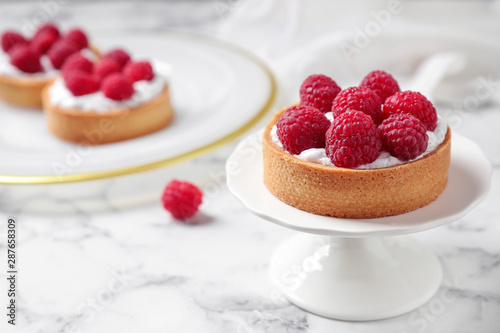 Cake stand with raspberry tart on marble table, space for text. Delicious pastries