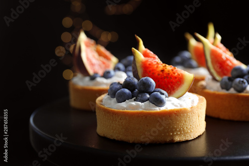 Tarts with blueberries and figs on black table against dark background, closeup. Delicious pastries