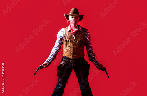 Man wearing cowboy hat, gun. West, guns. Portrait of a cowboy. owboy with weapon on red background. American bandit in mask, western man with hat. Portrait of farmer or cowboy in hat