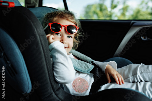 little cute girl in cap sitting in the car in child safety seat