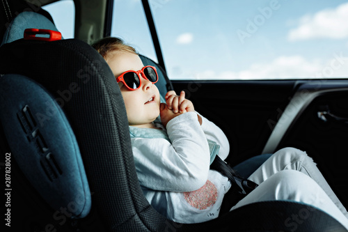 little cute girl in cap sitting in the car in child safety seat