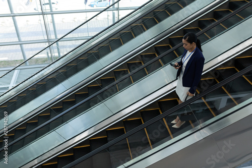 Businesswoman using mobile phone while moving down on escalator 