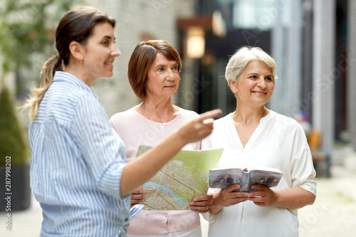 tourism, travel and friendship concept - female passerby showing direction to senior women with city guide and map on tallinn street