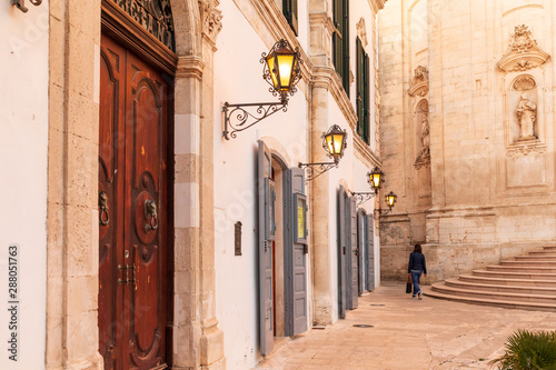 Italy, Apulia, Province of Taranto, Martina Franca. May 29, 2019. Piazza Maria Immacolata: person walking past Cathedral of Saint Martin; Basilica di San Martino.