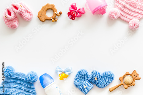 Blue and pink knitted footwear, hat, dummy, rattle and bottle frame for baby on white background top view mockup