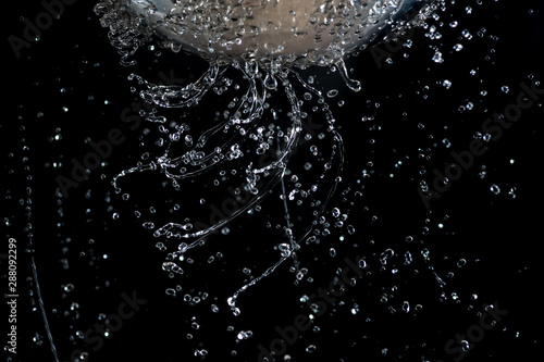 Flow and drops of water through holes in a colander on a dark background