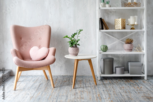 Stylish pink armchair with heart shaped pillow in a bright minimalist interior
