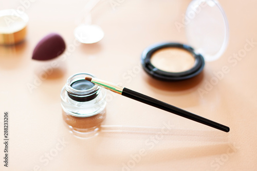 Black Gel eyeliner close up with a make up brush on the beige background