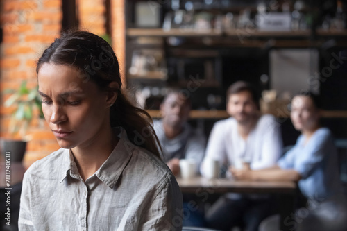 Upset mixed race woman suffering from bullying, sitting alone in cafe