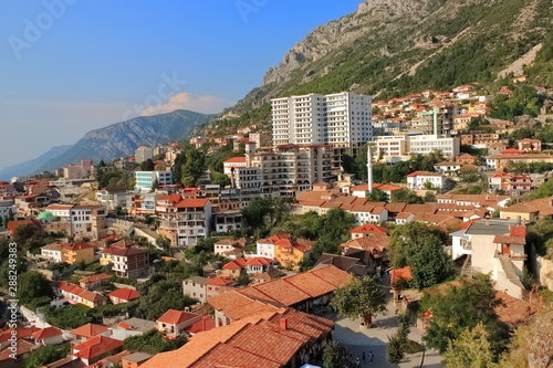 Panorama miasta Kruja w centralnej Albanii ze wzgórza ze średniowieczną cytadelą z widokiem na nowoczesne budynki mieszkalne na tle gór.