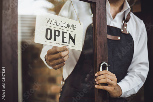 Store owner turning open sign broad through the door glass and ready to service.