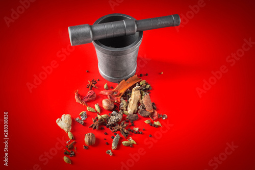 MACRO SHOT OF GARAM MASALA ON RED BACKGROUND WITH MORTAR AND PESTLE