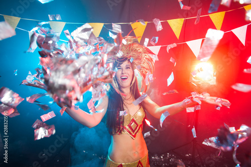 Cabaret, dancer and holidays concept - Cute young girl in bright colorful carnival costume on dark background