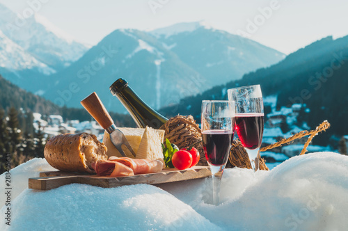 Traditional Italian food and drink outdoor in sunny winter day. Romantic alpine picnic in Madonna Di Campiglio with mountains background, Lambrusco cheese baguette tomatoes on the snow.