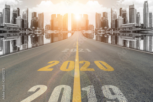 The number 2020 symbol represents the new year on the road heading to the city with beautiful skyscrapers background, New Year's and business target concepts.