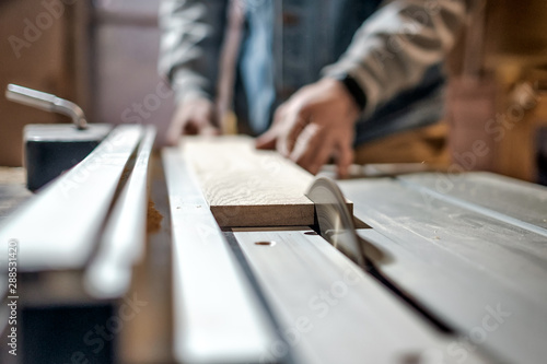 Caucasian man making wooden parts for custom furniture on machine tool called thickness planer in carpentry. Producing lumber concept