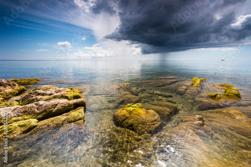 crystal clear water with green mossy stones at Lake Malawi, dark stormy clouds in the sky, Africa