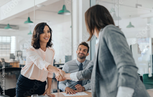 Smiling young businesswoman shaking hands with an office colleague