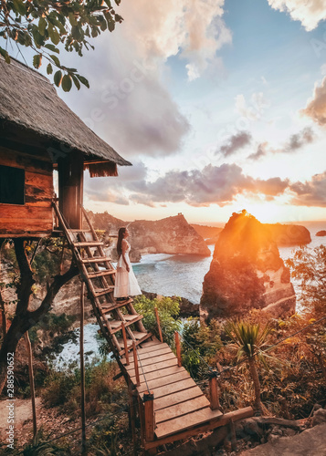 Travel woman looking sunrise view Tree House with Daimond beach, Nusa Penida island Bali ,Indonesia