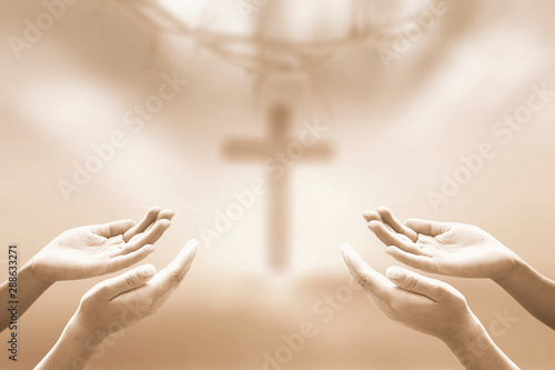 Worship concept: Two human hands praying over blurred crown of thorns and the cross on a sunset background
