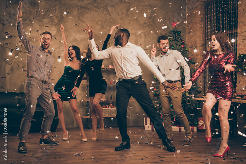 Full length photo of cheerful multinational buddies dance enjoy christmas party x-mas holidays in house with confetti newyear illumination indoors