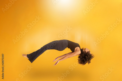 Side view of afro hair woman in zero gravity or being abducted by a UFO. Girl is flying or floating in the air. Side view of person. Over yellow background. Spiritism. Rising to the heaven.