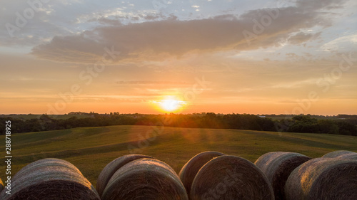 Sunrise over rows of round hay bales in a rural countryside field