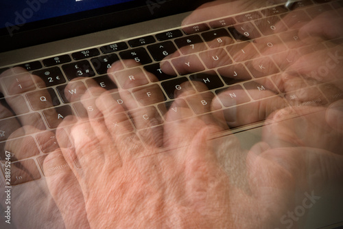 Laptop computer keyboard with blurred fingers of mans hand typing