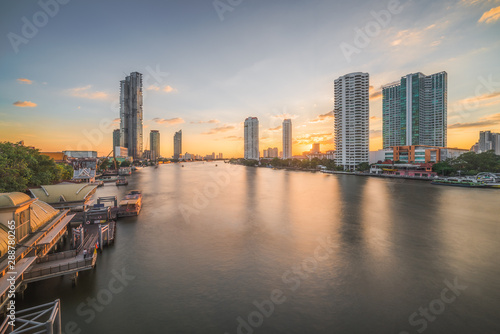 Chao Phraya River with Skyscrapers and Sathon Pier at Sunset as Seen from Taksin Bridge in Bangkok, Thailand