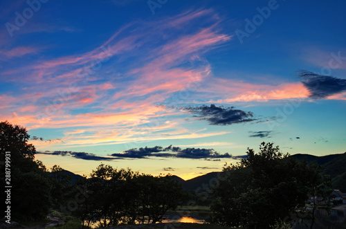 Dramatic sunset and sunrise sky with beautiful pink, yellow and blue clouds over the river and mountains