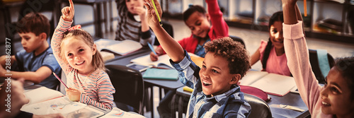 Schoolkids raising their hands in classroom