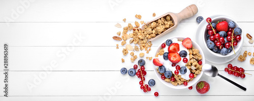 Breakfast with yogurt, muesli and berries on white wood background, top view, space for text.