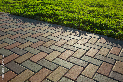 Colorful cobblestone road pavement and lawn divided by a concrete curb. Backlight.