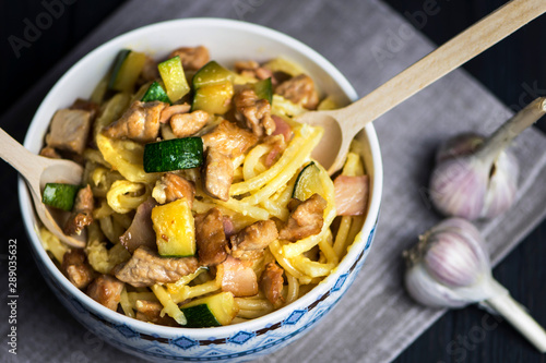 carbonara pasta with bacon, meat and zucchini in a bowl on a dark background
