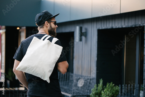 Young man holding white textile eco bag against urban city background. Ecology or environment protection concept. White eco bag for mock up.