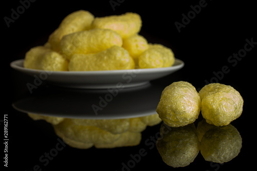 Lot of whole salted yellow corn puff on white ceramic plate isolated on black glass